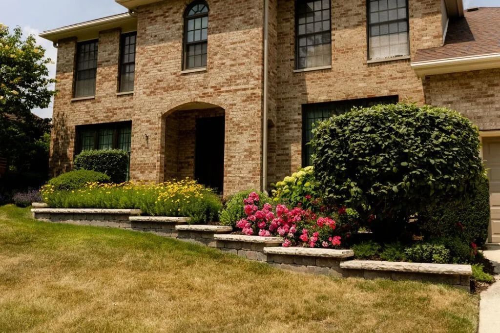 Brick house with tiered landscaping beds featuring flowers; front yard.