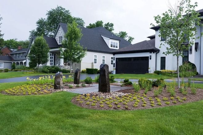A modern white house with a black garage door, lawn, and landscaped garden with stone pillars.