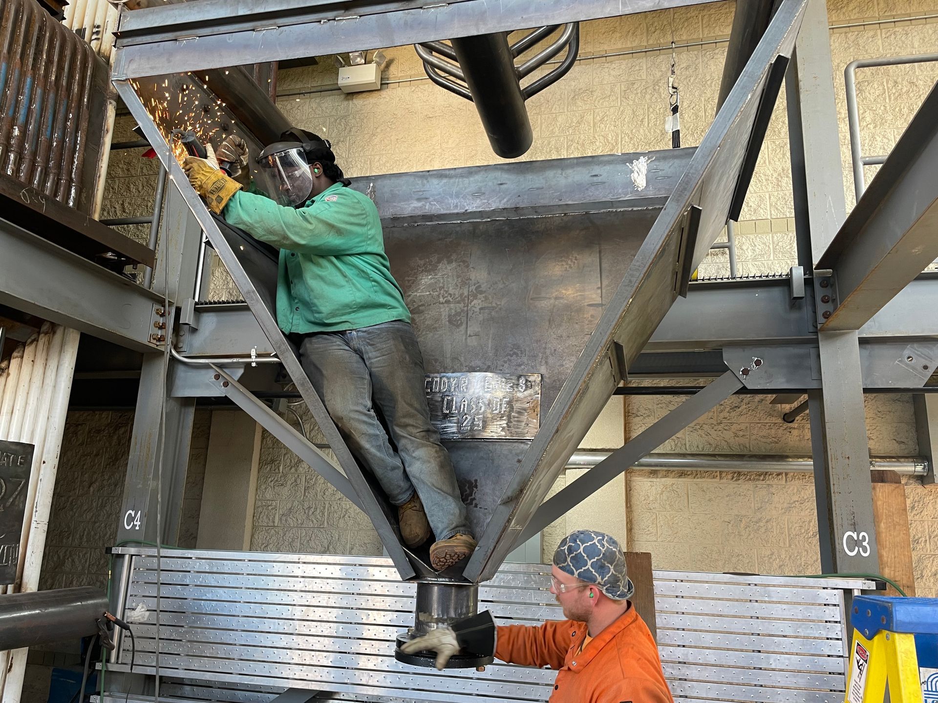 A man in a green jacket is working on a metal structure.