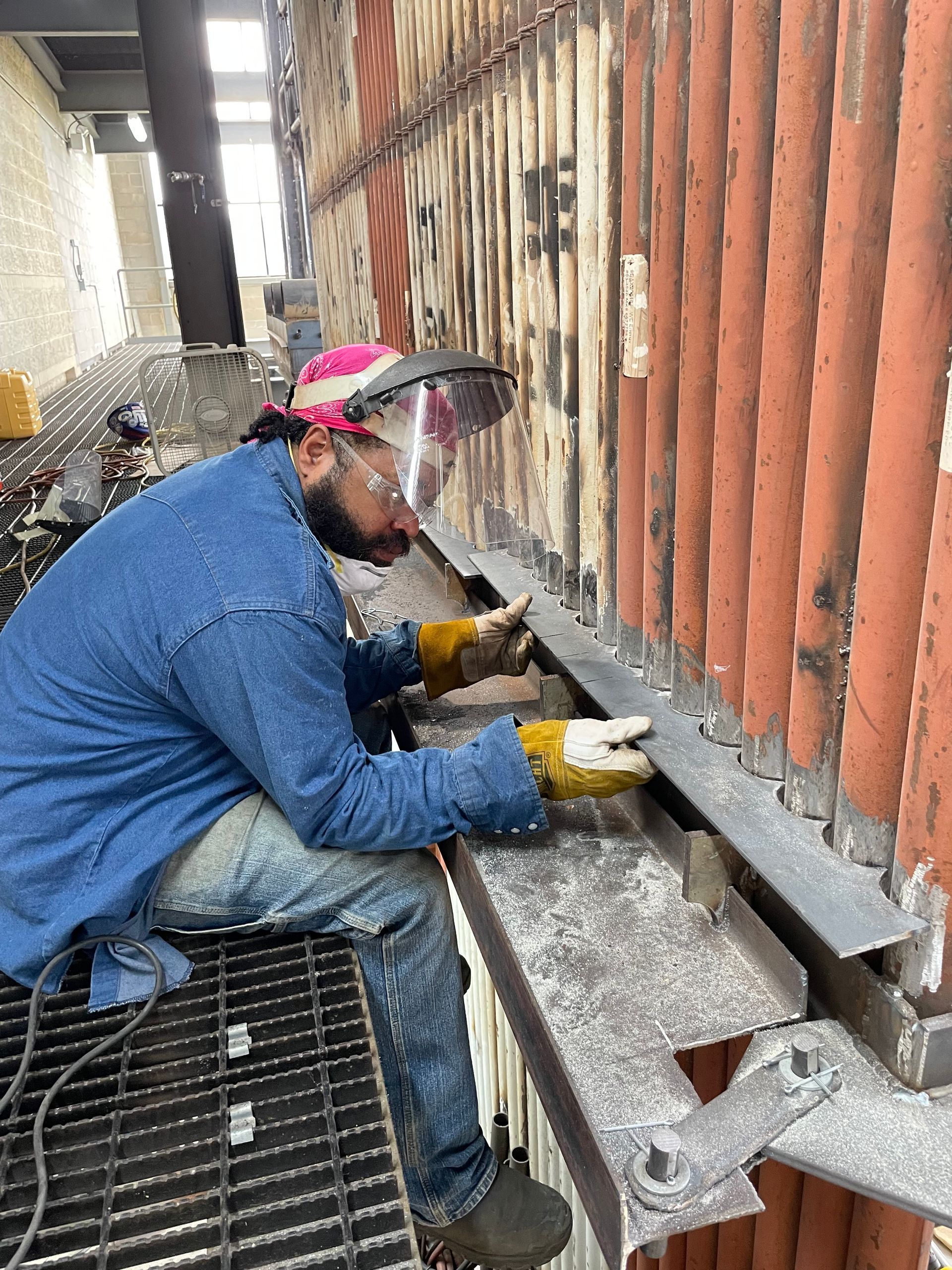 A man wearing a welding helmet is working on a metal structure.