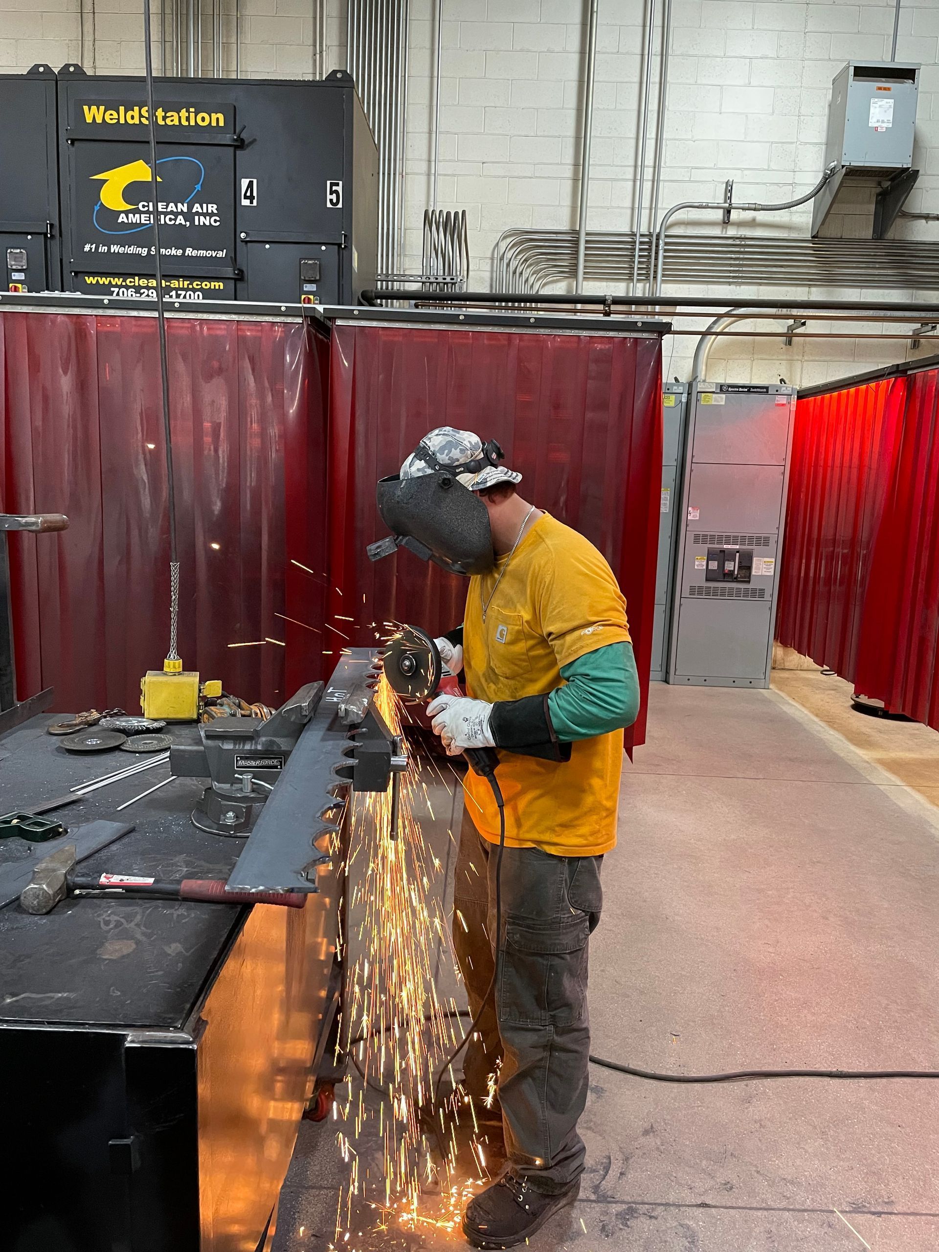 A man is cutting a piece of metal with a grinder in a factory.