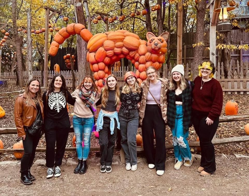 Group of friends posing in front of a pumpkin cat sculpture at a fall festival.