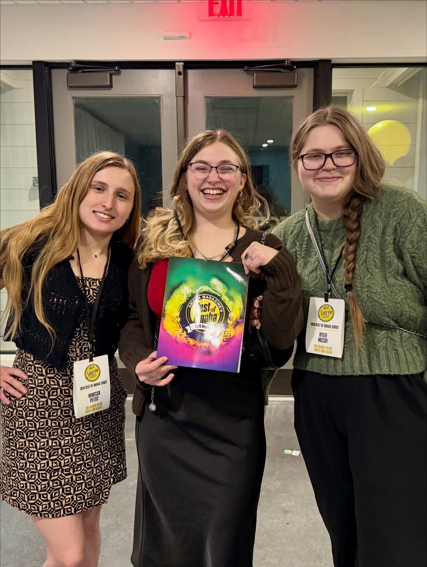 Three people smiling, holding colorful paper in front of doors with 