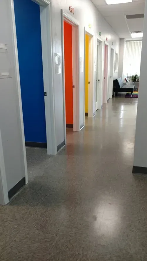 Hallway with doors painted blue, orange, yellow, white, and pink.