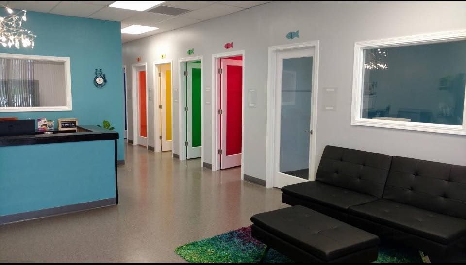Hallway with colorful doors, teal reception desk, black couch, and bright green and blue rug.