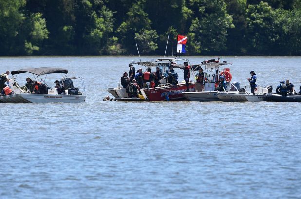 Boats on water with people in life vests; flag on the middle boat. Lush trees in the background.