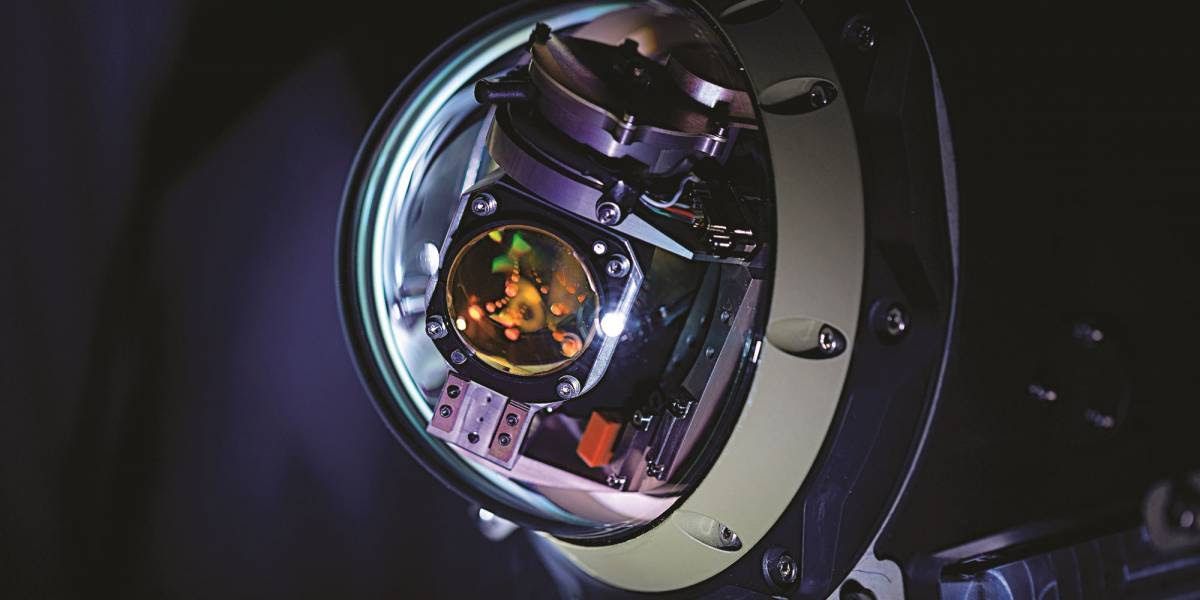 Close-up of a complex mechanical device with multiple components, visible through a circular frame, set against a dark background.