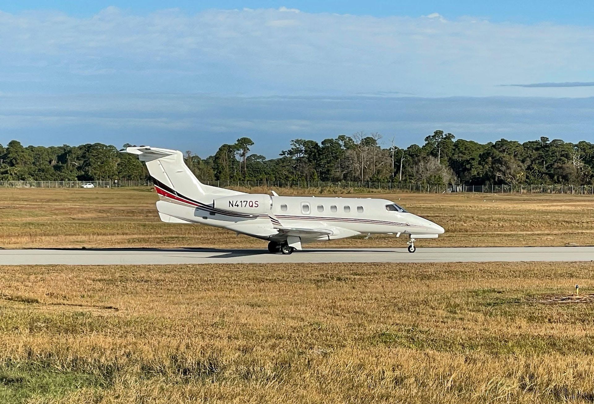 A private jet on a runway with trees and blue sky in the background.