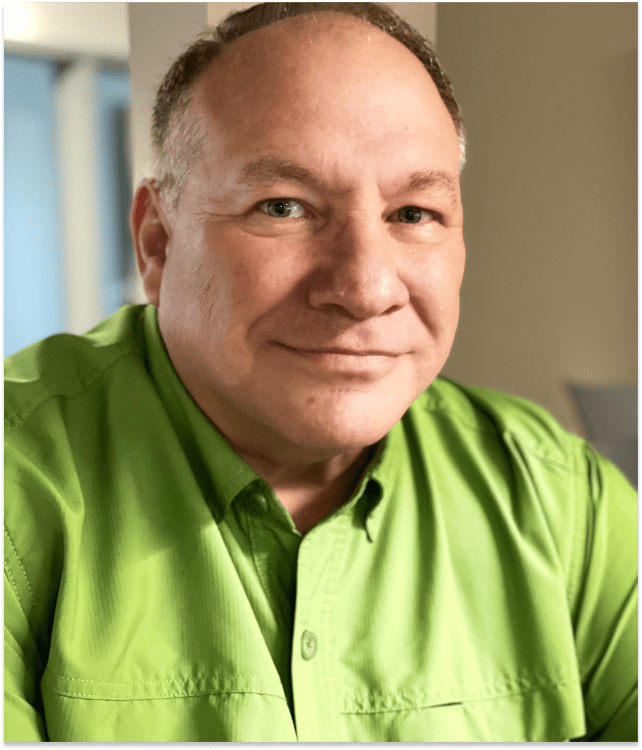 Man with short hair wearing a green shirt, smiling slightly indoors.