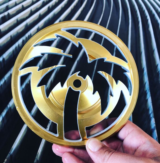 Gold and black circular design with a palm tree cut-out, held in hand.