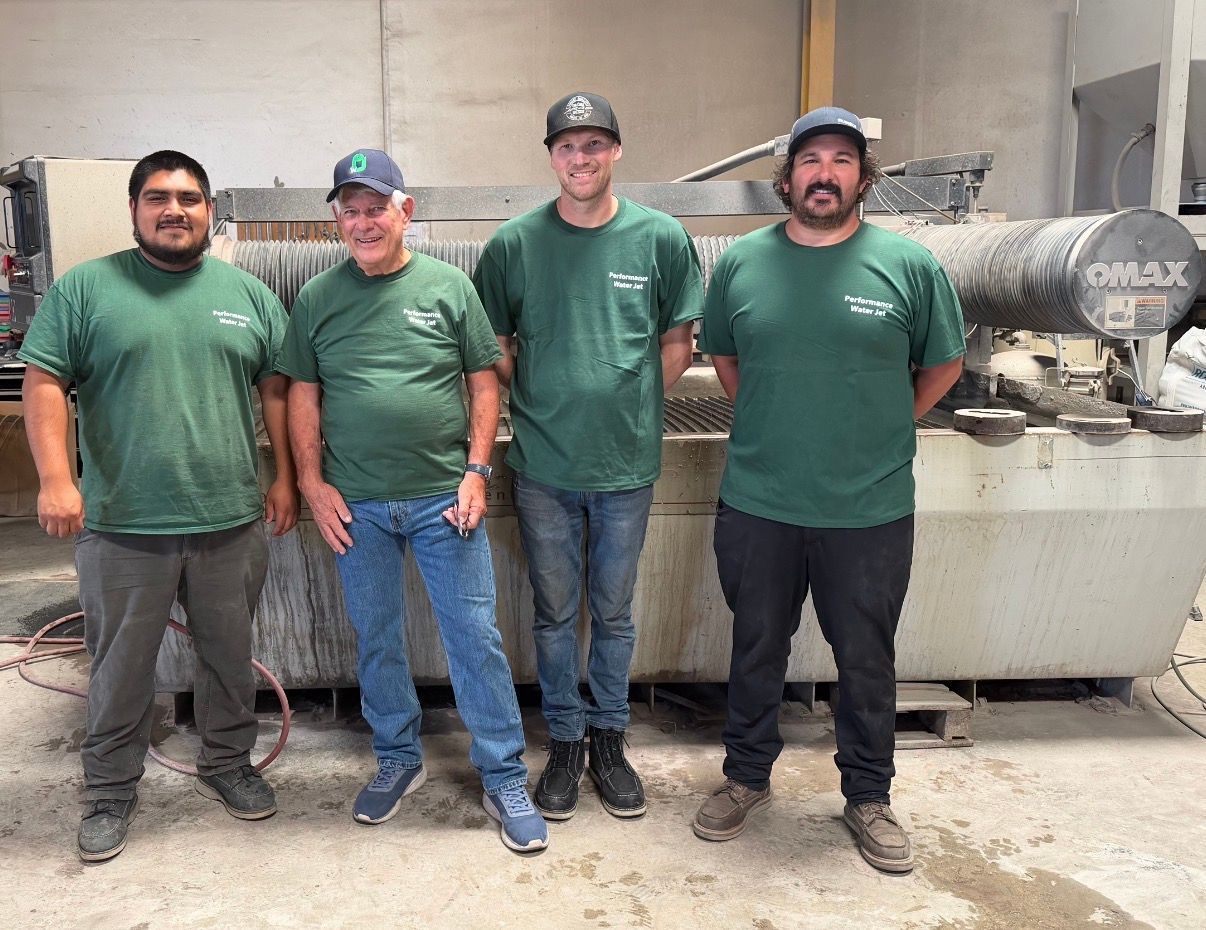 Four workers in green shirts stand in a dusty industrial workshop beside machinery.