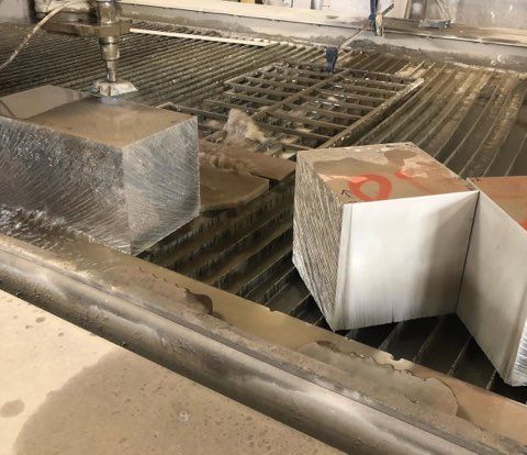 A water jet cutting a metal block in an industrial setting. Wet, metallic surfaces are visible.