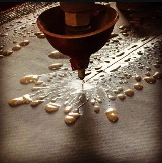A nozzle spraying gold-colored liquid onto a surface, creating droplets.