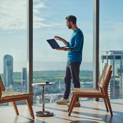 Man standing with a laptop in a bright high-rise office with city skyline views
