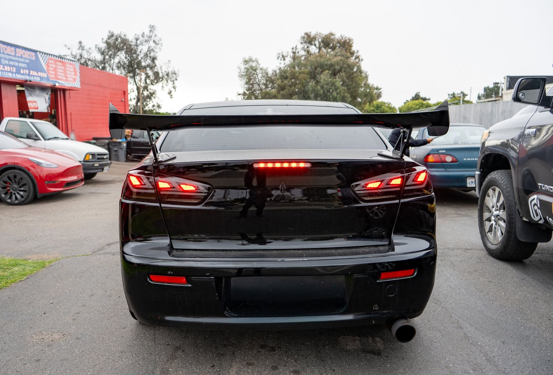 Black sports car viewed from the rear with brake lights on in a parking lot on a rainy day