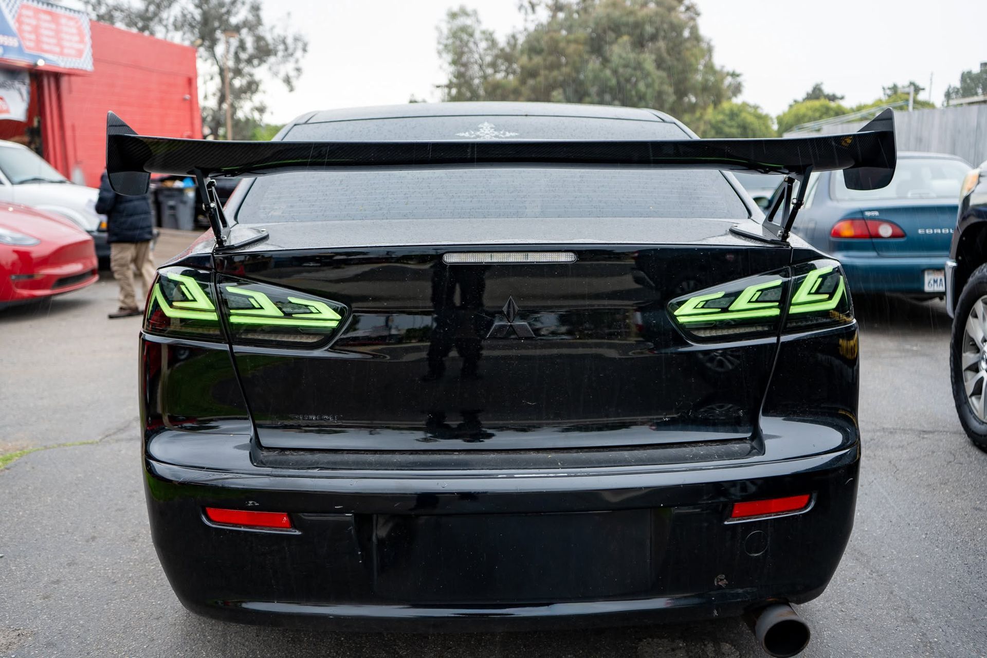 Rear view of a black sports sedan with green taillights and a large rear spoiler in a parking lot
