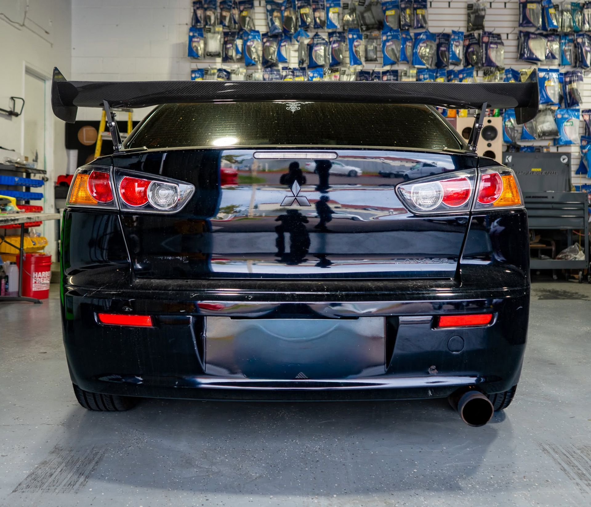 Rear view of a black sedan parked in a garage, with a large rear spoiler and red taillights.