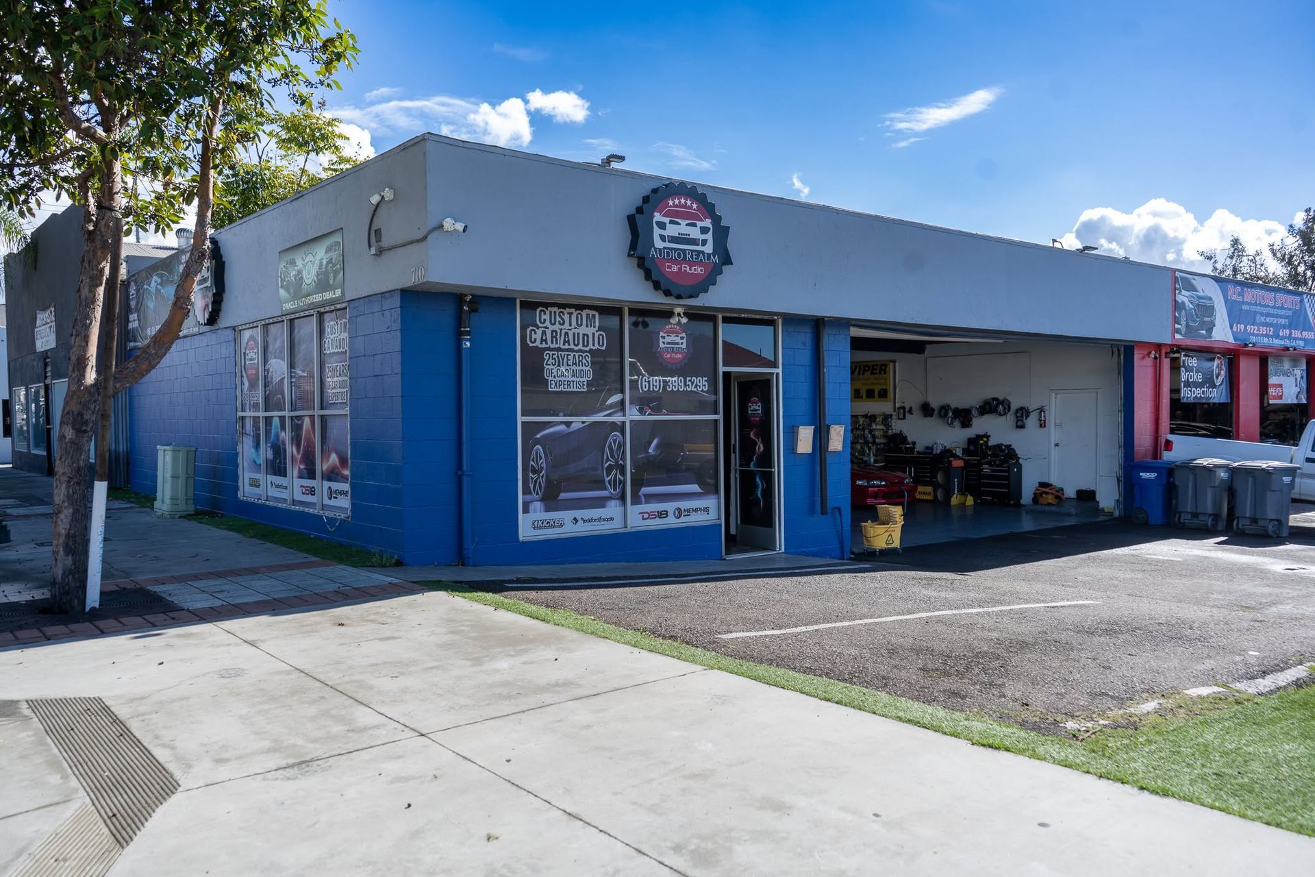 Blue storefront with large windows, open garage bay, and bicycles outside on a sunny street corner