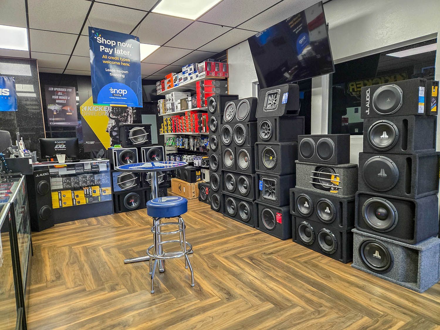 Audio store showroom with stacked speakers, TVs, and a blue stool in the center