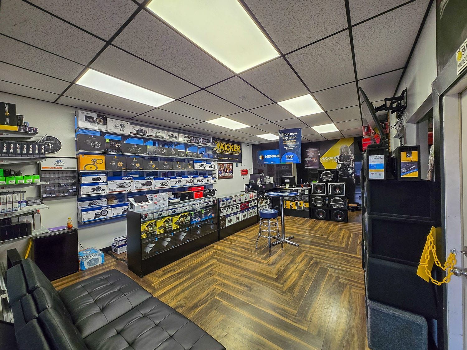 Electronics store interior with gaming consoles, display cases, and a black couch on a wood floor.
