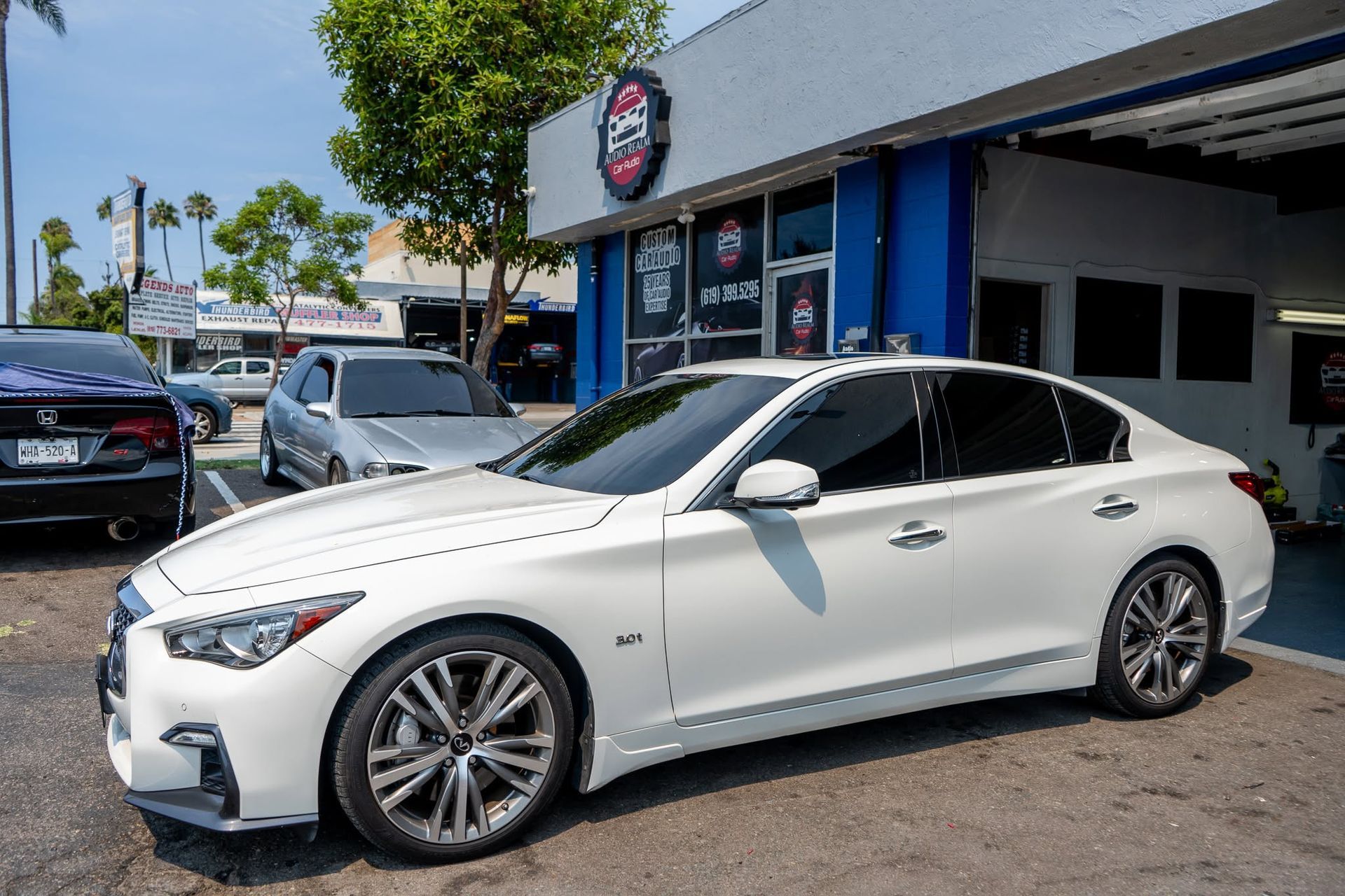 White sedan parked outside a storefront on a sunny street.