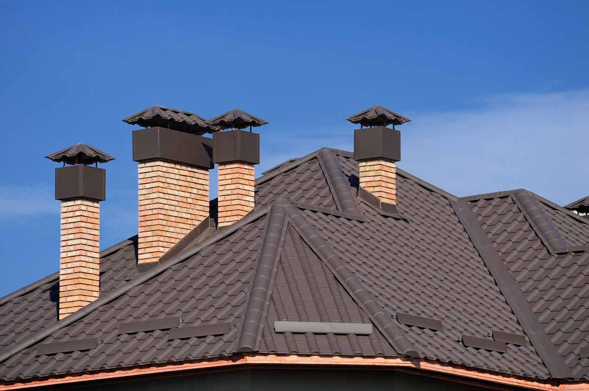 Brown metal roof with brick chimneys against a blue sky.