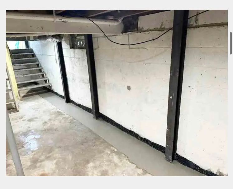 Basement foundation wall reinforced with vertical black steel beams and a freshly poured concrete floor edge.