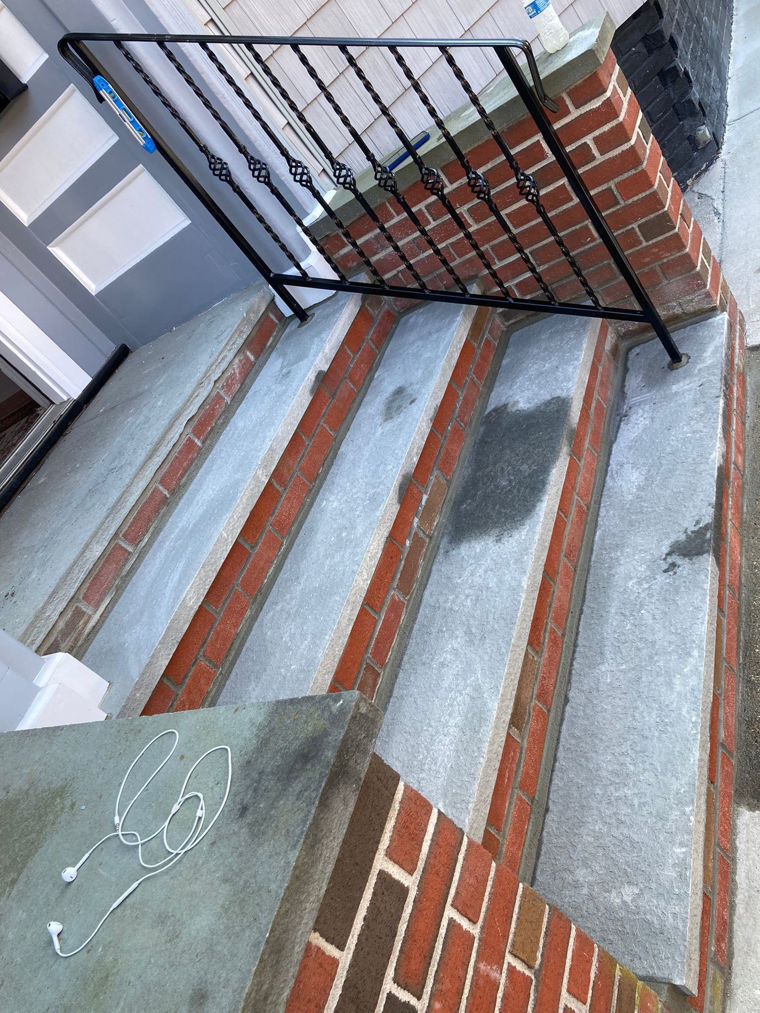 Brick steps leading to a gray door. Black iron railing on right side. White lights on the bottom step.