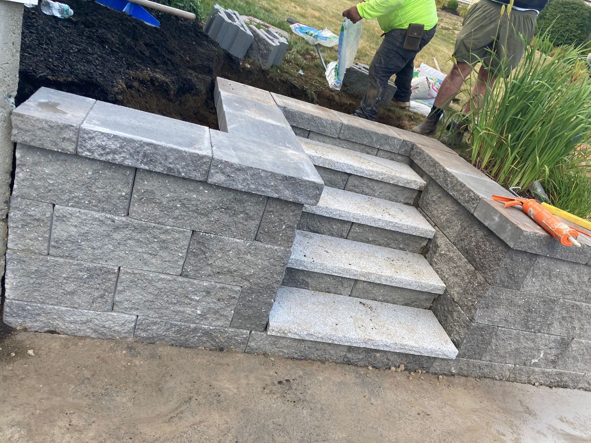 Construction workers building stone steps and a retaining wall outdoors.