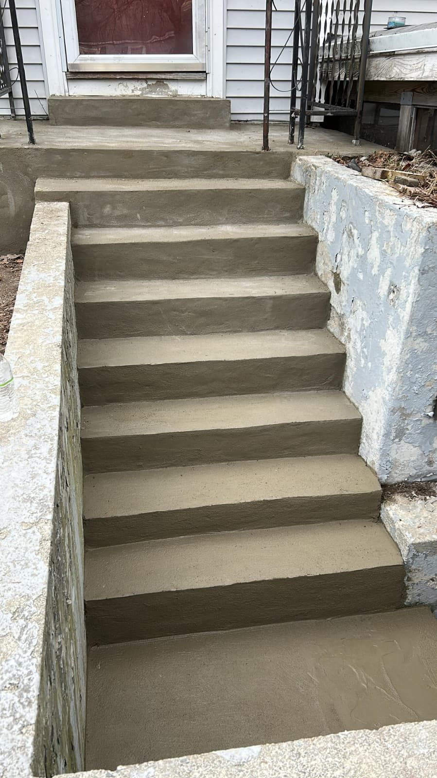 Concrete outdoor stairs leading up to a front door between retaining walls.