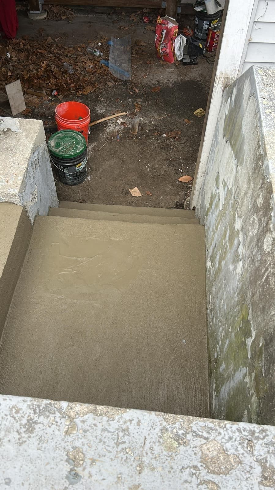 Concrete basement stairs leading down to a dirt floor with two red and green buckets in the background
