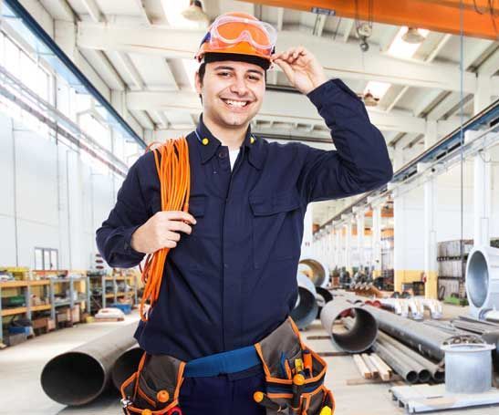 A man wearing a hard hat and goggles is smiling in a factory