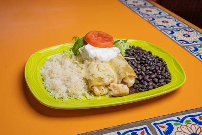 A plate of food with rice , beans and enchiladas on a table.