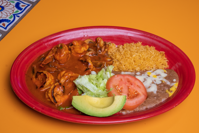 A red plate topped with shrimp, rice, beans, and avocado on a yellow table.