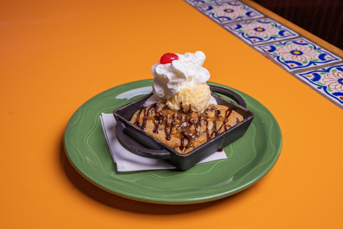 A green plate topped with a dessert with whipped cream and a cherry on top.