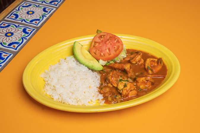 A yellow plate topped with rice, tomatoes, and avocado on a table.