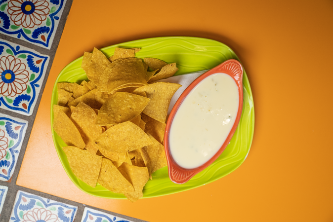 A plate of nachos and a bowl of cheese dip on a table.