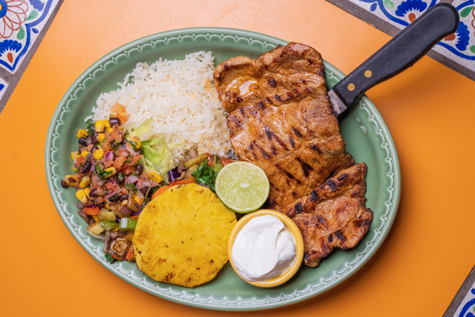 A plate of food with meat, rice, vegetables, and sour cream on a table.