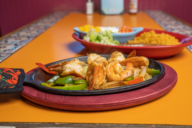 A plate of shrimp and vegetables on a sizzling pan on a table.