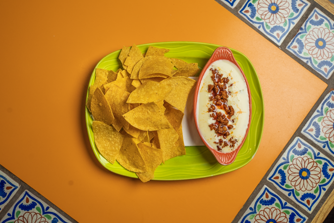 A plate of nachos and a bowl of cheese dip on a table.