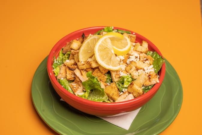 A salad with chicken, lettuce, croutons, and lemon slices on a green plate.