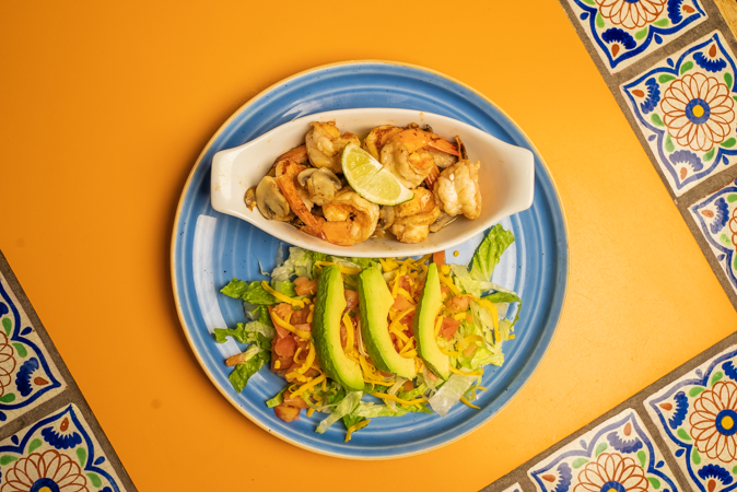 A plate of food with shrimp, avocado, and lettuce on a table.