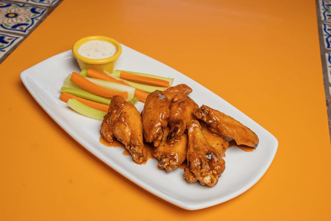 A white plate topped with chicken wings and vegetables on an orange table.