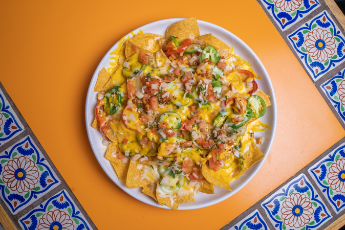 A plate of nachos is sitting on a tiled table.