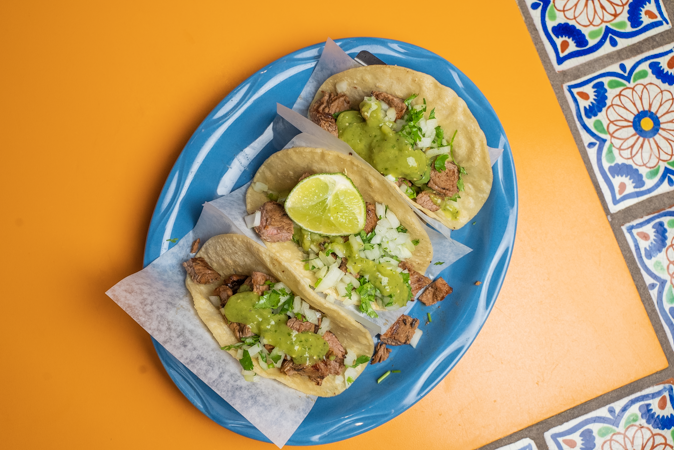 A blue plate topped with three tacos on a table.