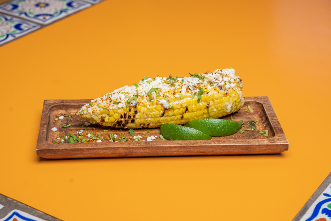 A piece of corn on the cob on a wooden cutting board on a table.