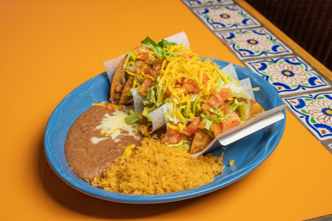 A blue plate topped with tacos, beans, and rice on a yellow table.