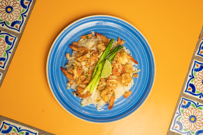 A blue plate topped with shrimp and rice on a yellow table.