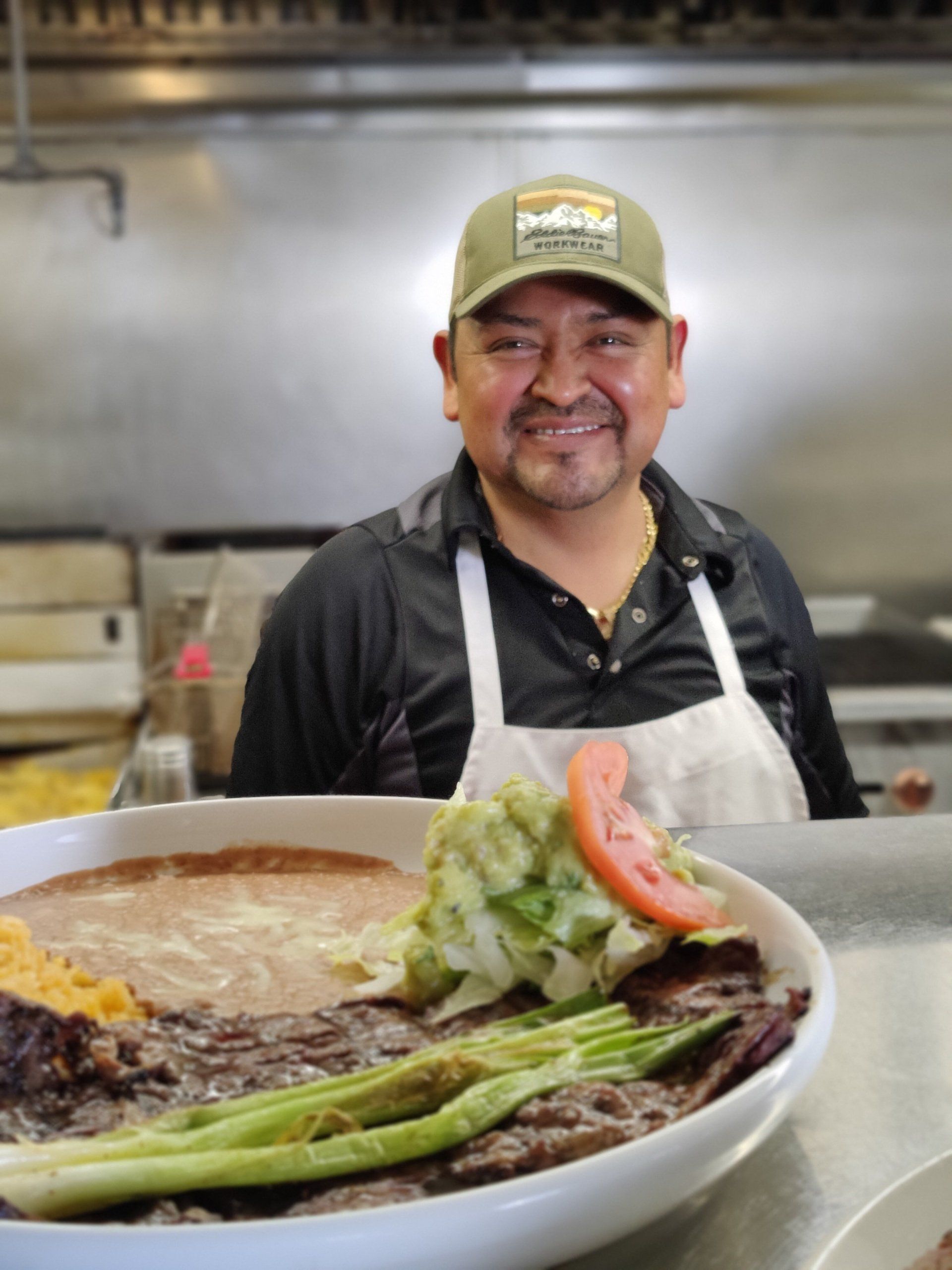 A man in an apron is smiling in front of a plate of food.
