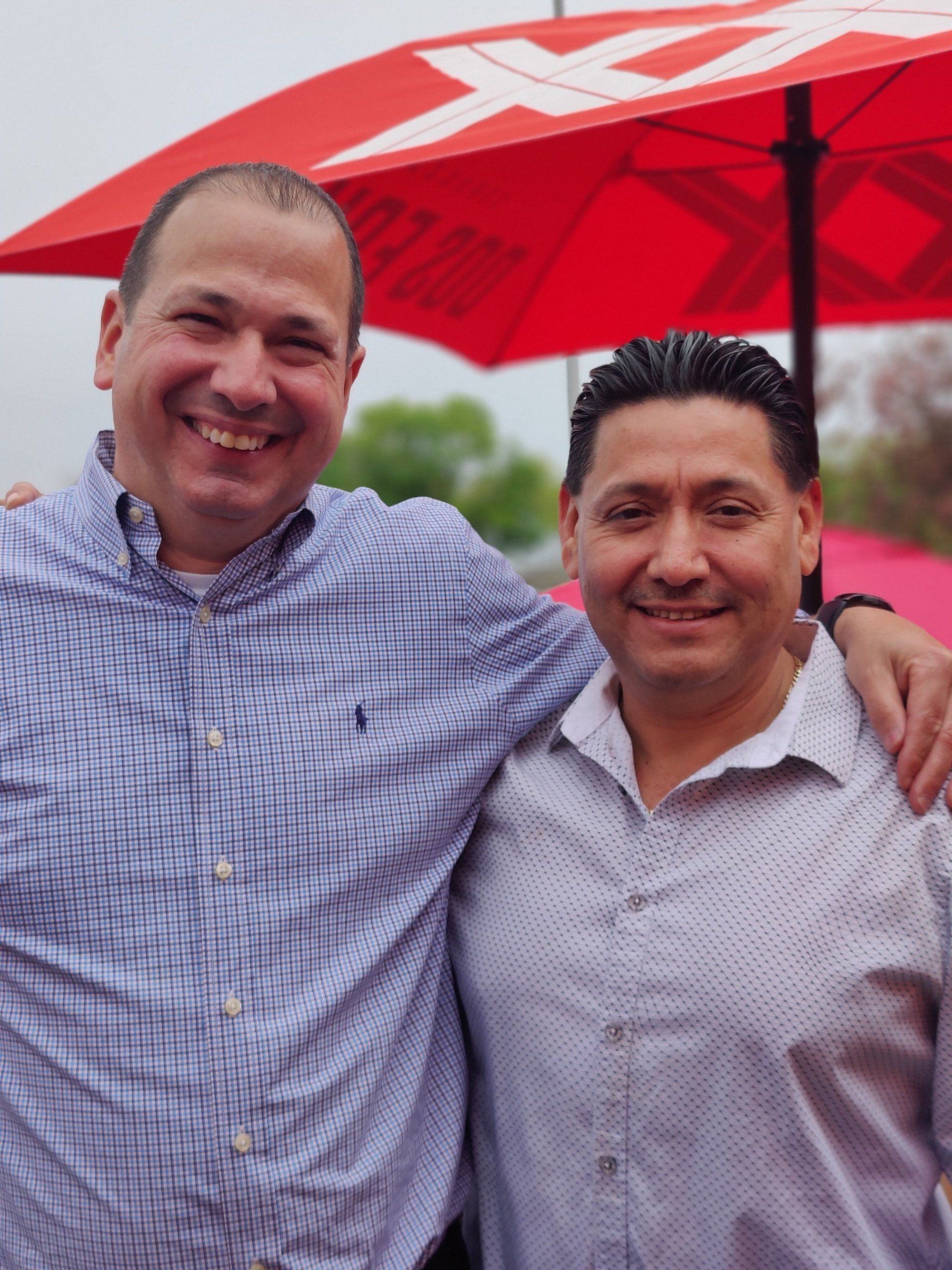 Two men are posing for a picture under a red umbrella